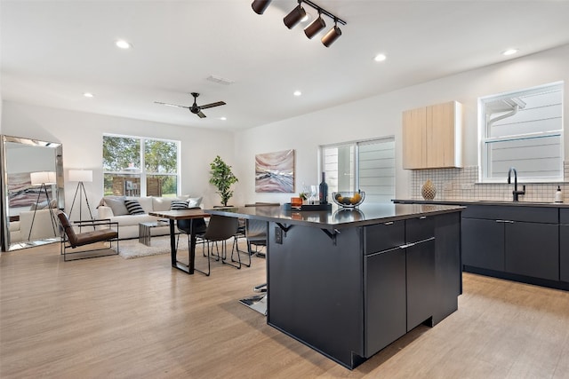 kitchen featuring a kitchen island, a breakfast bar, sink, ceiling fan, and light wood-type flooring