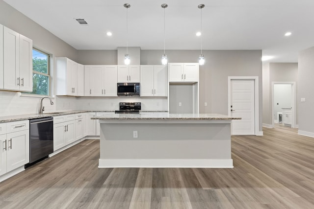 kitchen featuring a kitchen island, hanging light fixtures, appliances with stainless steel finishes, light stone counters, and light hardwood / wood-style floors