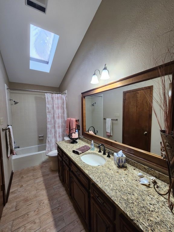 full bathroom featuring vaulted ceiling with skylight, toilet, hardwood / wood-style floors, vanity, and shower / bath combo with shower curtain