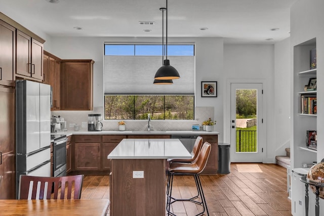 kitchen featuring a center island, decorative light fixtures, stainless steel appliances, sink, and wood-type flooring