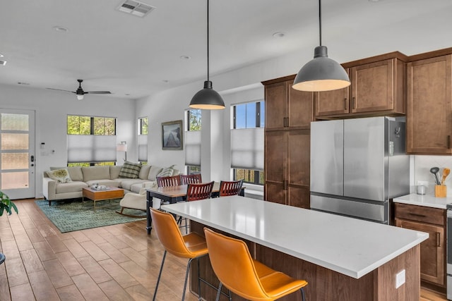 kitchen featuring decorative light fixtures, light wood-type flooring, stainless steel refrigerator, a kitchen breakfast bar, and ceiling fan