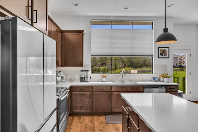 kitchen featuring appliances with stainless steel finishes, hanging light fixtures, decorative backsplash, and light hardwood / wood-style floors