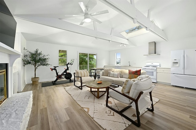 living room featuring ceiling fan, a skylight, high vaulted ceiling, a fireplace, and light hardwood / wood-style floors