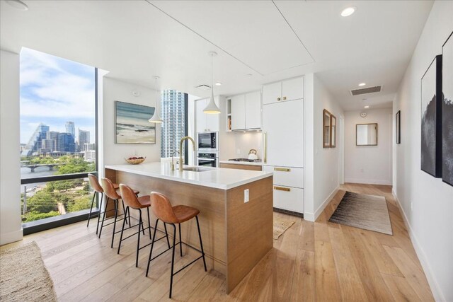 kitchen with a kitchen breakfast bar, light hardwood / wood-style flooring, hanging light fixtures, stainless steel appliances, and white cabinets