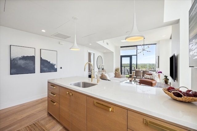 kitchen with decorative light fixtures, light stone counters, light wood-type flooring, and sink