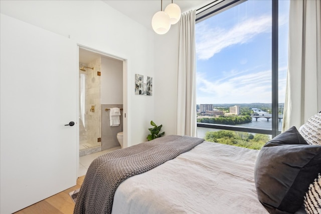 bedroom with connected bathroom, a water view, and light hardwood / wood-style floors