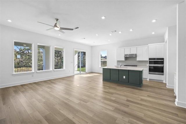 kitchen with light wood-type flooring, ceiling fan, sink, white cabinets, and an island with sink