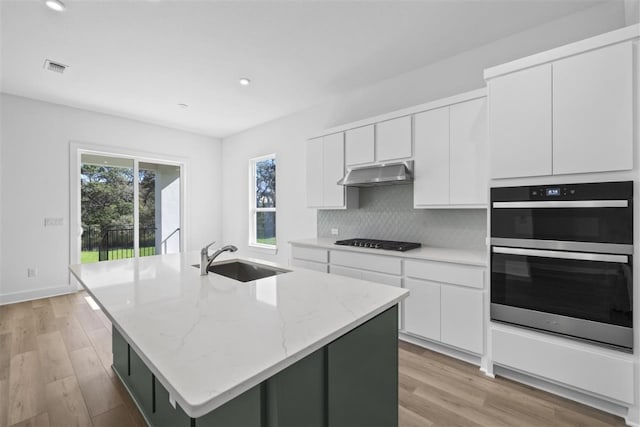 kitchen with a center island with sink, black gas stovetop, sink, double oven, and white cabinetry