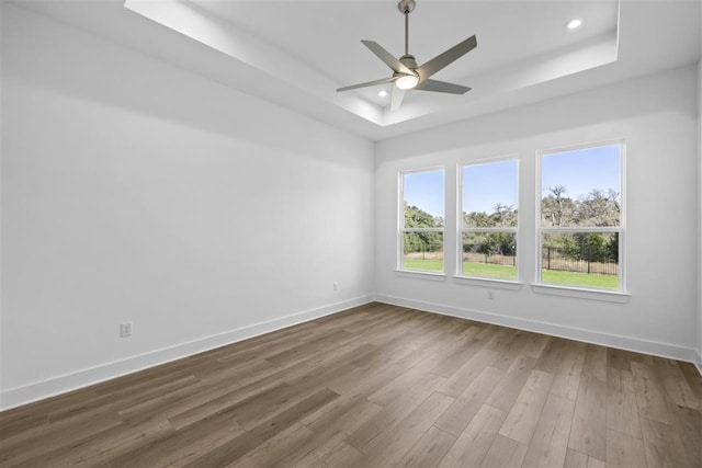 empty room with hardwood / wood-style floors, a tray ceiling, and ceiling fan