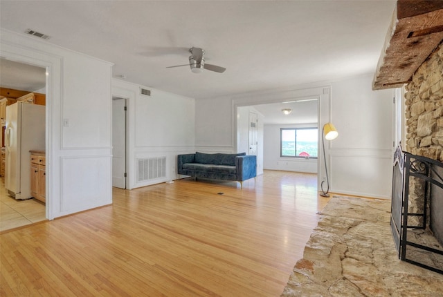 unfurnished living room featuring light hardwood / wood-style flooring, ceiling fan, and a stone fireplace