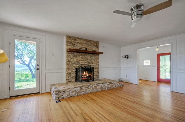 unfurnished living room with light wood-type flooring, ceiling fan, and a stone fireplace