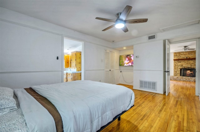 bedroom featuring a stone fireplace, ceiling fan, and light hardwood / wood-style flooring