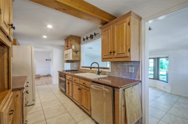 kitchen featuring dark stone countertops, light wood-type flooring, beamed ceiling, sink, and appliances with stainless steel finishes