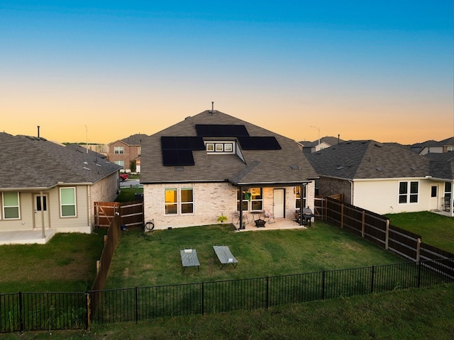 back house at dusk featuring solar panels, a patio area, and a lawn