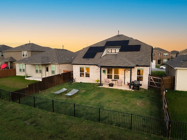 back house at dusk with solar panels, a patio area, and a lawn