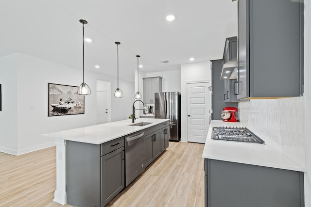 kitchen featuring sink, stainless steel appliances, decorative light fixtures, gray cabinets, and a center island with sink