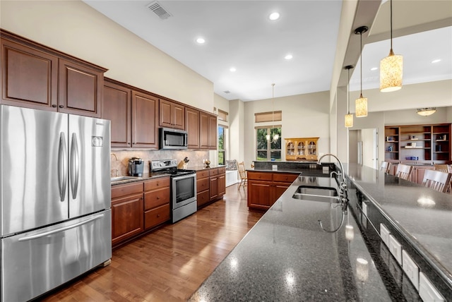 kitchen featuring hanging light fixtures, sink, stainless steel appliances, dark hardwood / wood-style floors, and dark stone countertops