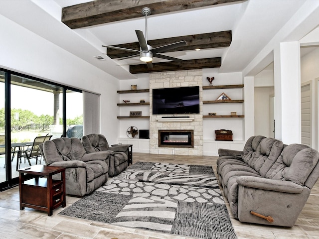 living room with a stone fireplace, ceiling fan, and beamed ceiling