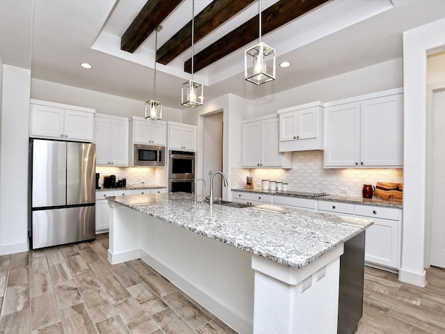 kitchen with stainless steel appliances, sink, a center island with sink, white cabinetry, and hanging light fixtures