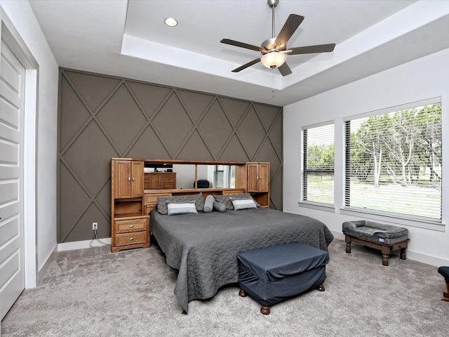 carpeted bedroom with a raised ceiling and ceiling fan