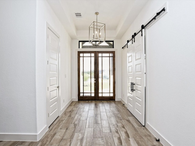 entrance foyer with a notable chandelier, a barn door, a raised ceiling, and french doors