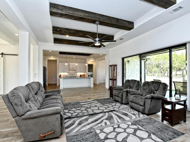 living room featuring a barn door, ceiling fan, beamed ceiling, and light hardwood / wood-style floors