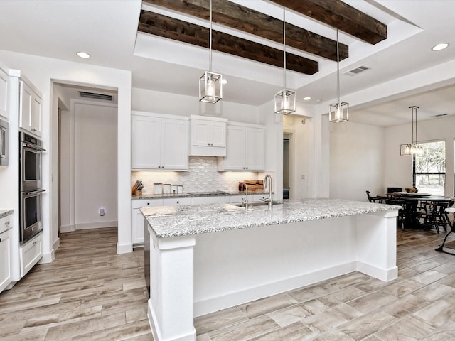 kitchen featuring stainless steel double oven, a center island with sink, white cabinetry, and sink