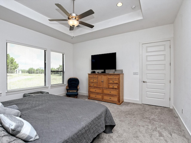 carpeted bedroom with a raised ceiling and ceiling fan