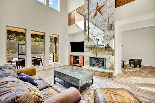 living room with wood-type flooring, a stone fireplace, and a towering ceiling