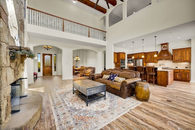 living area with a high ceiling, light wood finished floors, arched walkways, and an inviting chandelier
