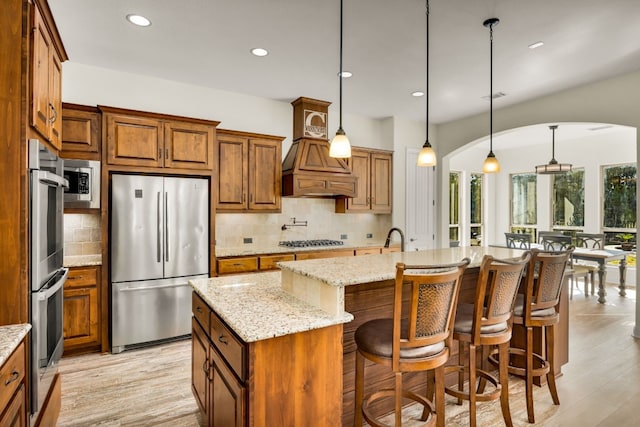 kitchen featuring a breakfast bar, light stone counters, stainless steel appliances, a center island with sink, and decorative light fixtures