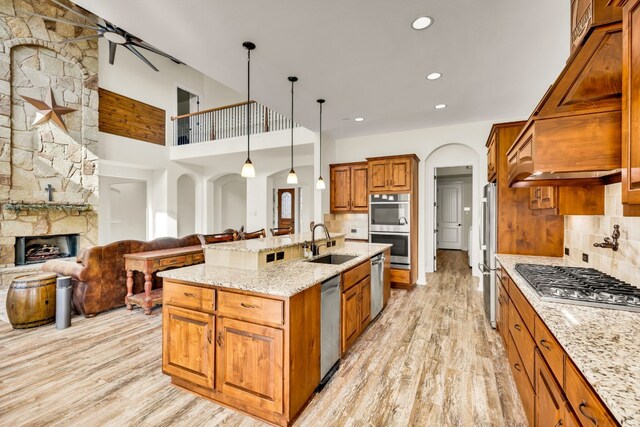 kitchen featuring an island with sink, light wood-style flooring, brown cabinetry, stainless steel appliances, and a sink