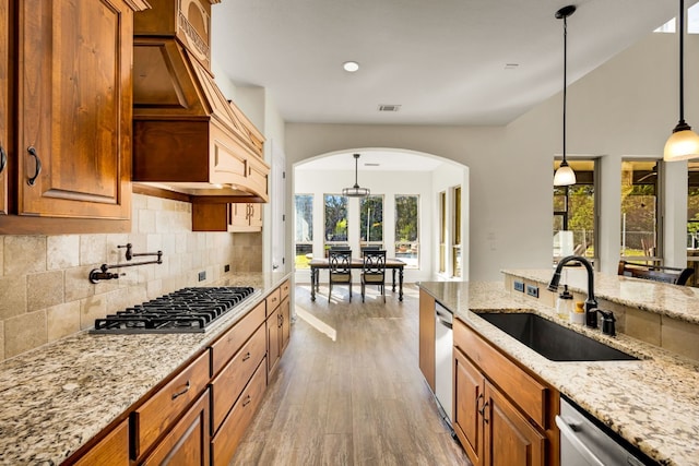kitchen featuring decorative backsplash, a sink, appliances with stainless steel finishes, arched walkways, and brown cabinetry