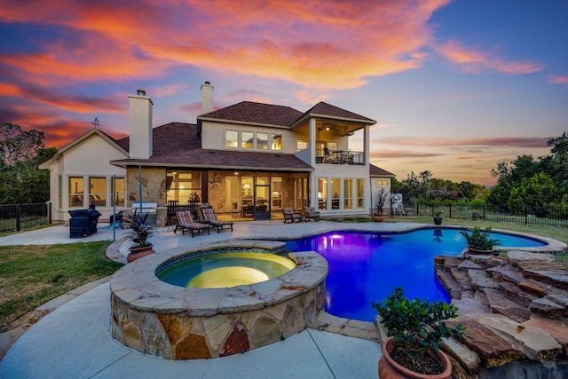 rear view of property with a balcony, a chimney, a patio area, a fenced backyard, and a pool with connected hot tub