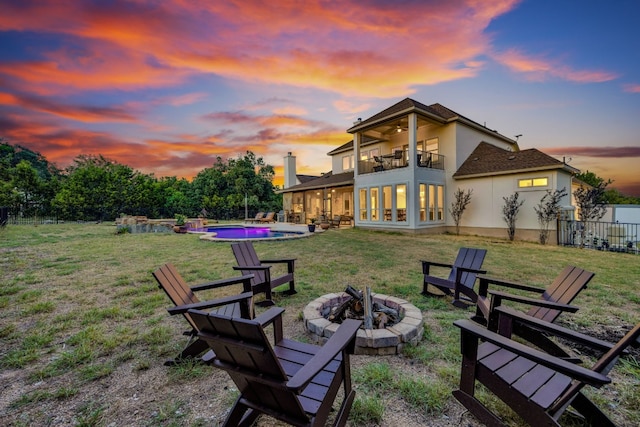 yard at dusk with a balcony, a fenced in pool, a patio area, and an outdoor fire pit