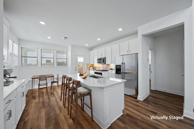 kitchen with appliances with stainless steel finishes, a wealth of natural light, sink, white cabinetry, and an island with sink