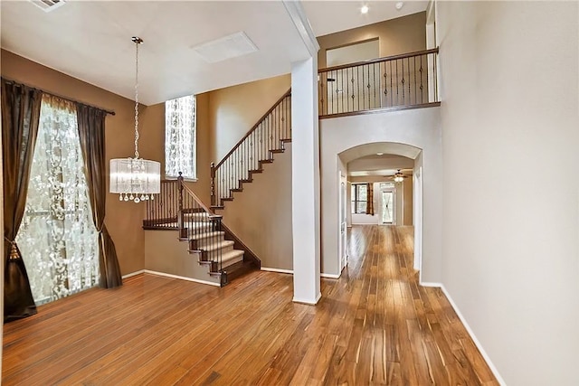 foyer with a towering ceiling, ceiling fan with notable chandelier, and hardwood / wood-style floors