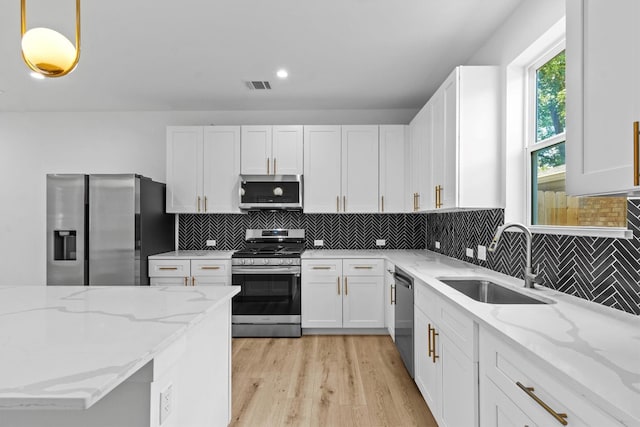 kitchen with white cabinets, decorative light fixtures, appliances with stainless steel finishes, light stone counters, and sink