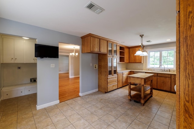 kitchen with light tile patterned floors, decorative light fixtures, sink, a kitchen island, and tasteful backsplash