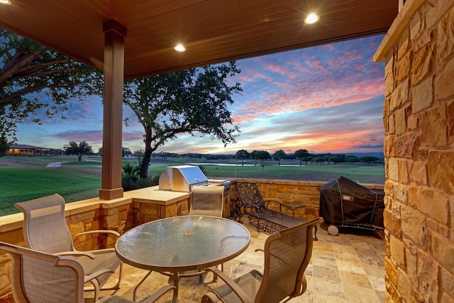 patio terrace at dusk featuring an outdoor kitchen and a grill