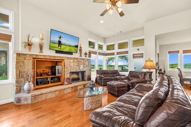 living room with ceiling fan, wood-type flooring, and a stone fireplace