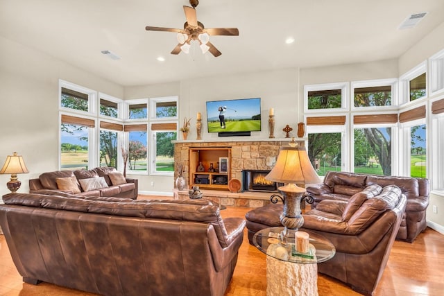 living room with a stone fireplace, light wood-type flooring, and ceiling fan