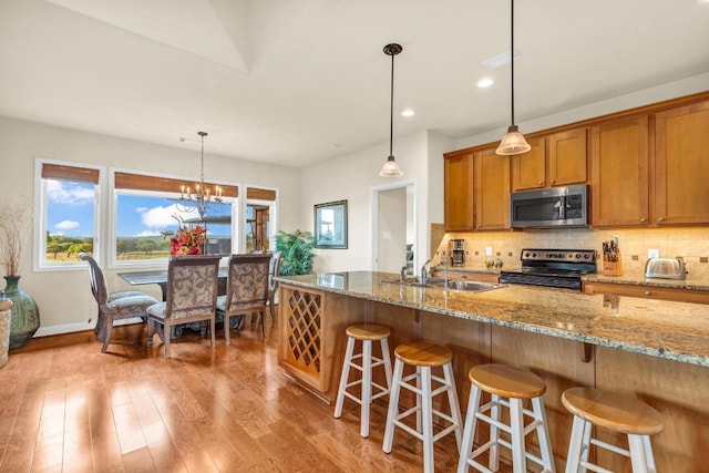 kitchen featuring light stone counters, stainless steel appliances, pendant lighting, light hardwood / wood-style floors, and a chandelier