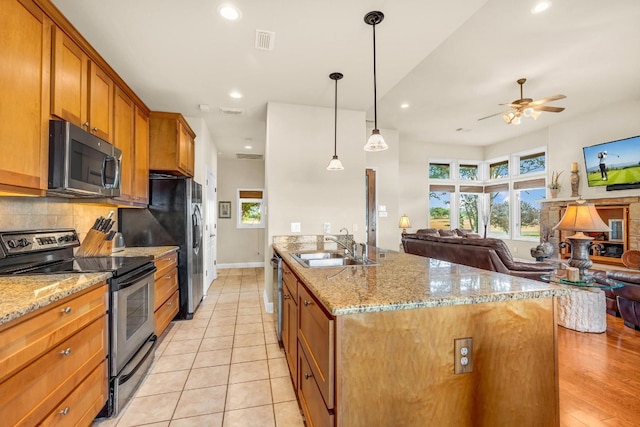 kitchen featuring stainless steel appliances, decorative light fixtures, sink, ceiling fan, and a kitchen island with sink