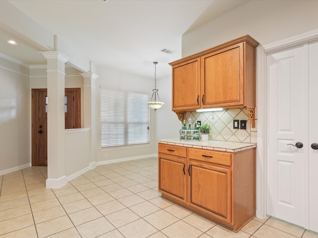 kitchen with tile countertops, ornate columns, ornamental molding, decorative backsplash, and light tile patterned flooring