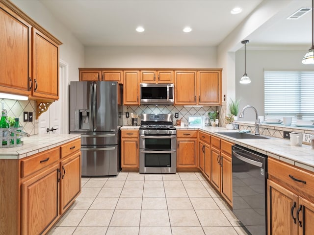 kitchen with pendant lighting, tasteful backsplash, tile counters, sink, and appliances with stainless steel finishes