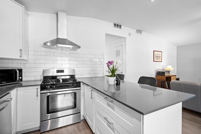 kitchen with wall chimney range hood, stainless steel appliances, kitchen peninsula, and white cabinetry