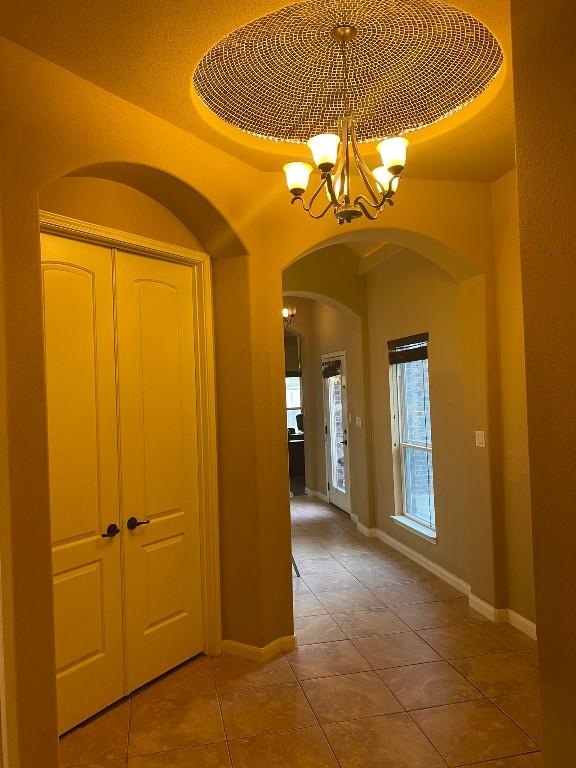 hallway with baseboards, a notable chandelier, and light tile patterned flooring