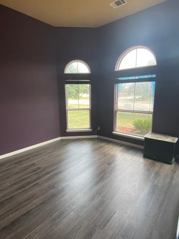 empty room with dark wood finished floors, visible vents, and baseboards