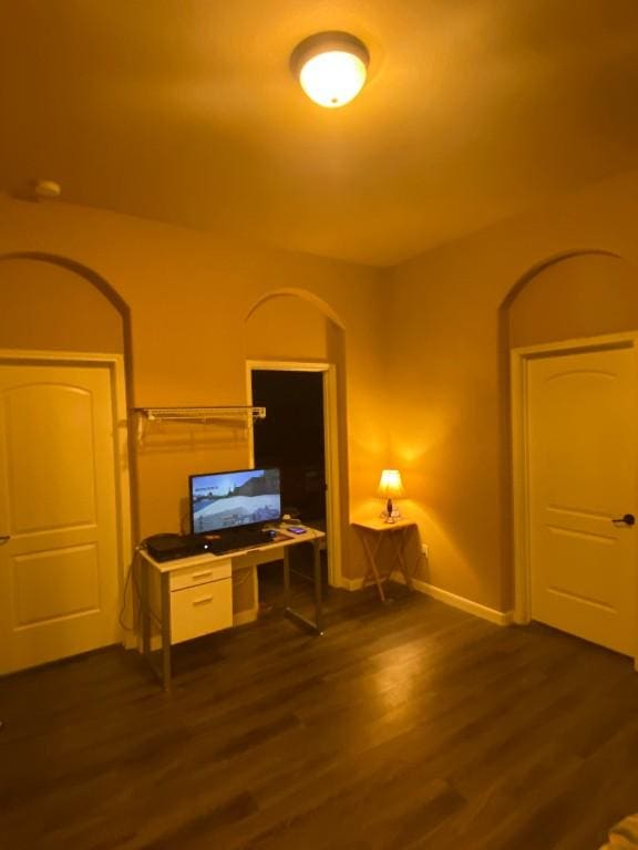 office area featuring dark wood-type flooring, baseboards, and arched walkways